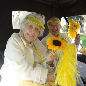 Two class of 1942 alumnae sit in an antique car, holding sunflowers