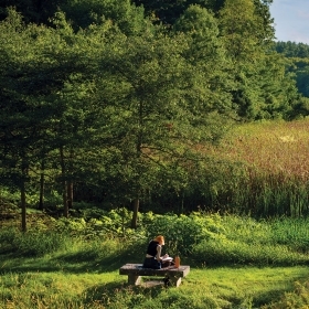 在阿勒奈谷，一名学生坐在长凳上学习，俯瞰湿地，远处是瓦班湖。