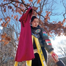 照片显示，24岁的艾玛·斯莱贝克是美国宇航局的主席，切罗基印第安人东部乐队的后裔，她把一件红色连衣裙挂在学院院落的树上，这是REDress装置的一部分。