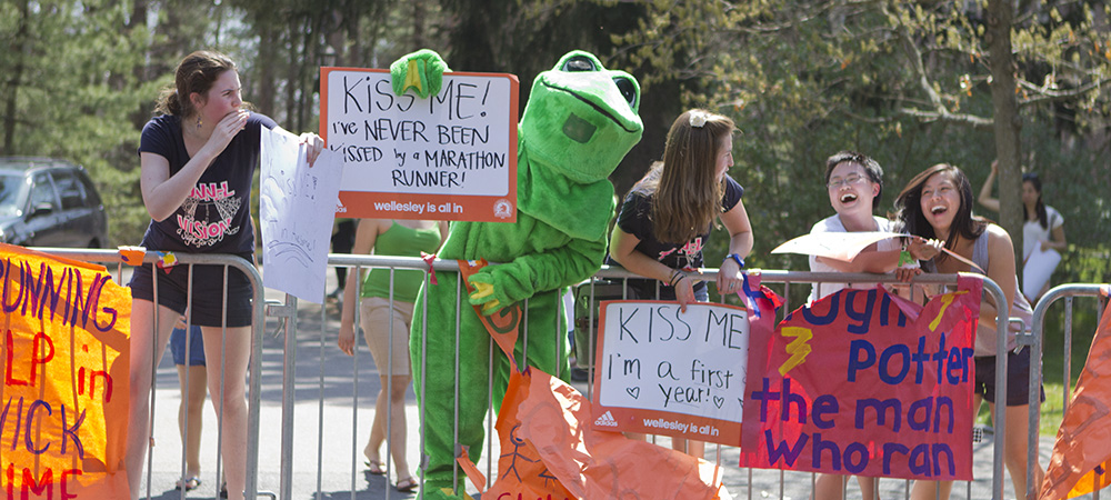 学生在青蛙服装和创造性标志上为跑步者欢呼