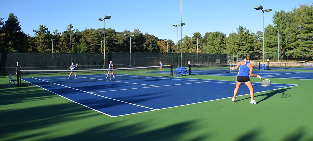 三名学生在硬庭上打网球。两个与另一侧的另一侧。