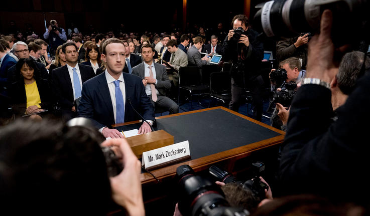 Mark Zuckerberg坐在会议上的一张桌子与围绕着他的媒体