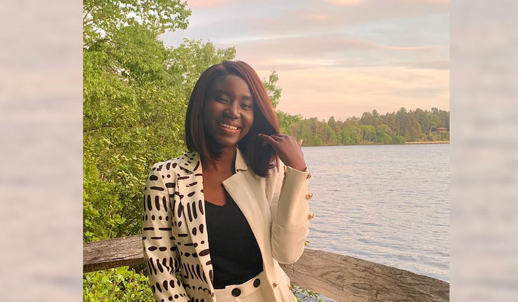 Adwoa Difie Antwi ’21 posing in front of Lake Waban with a sunset sky