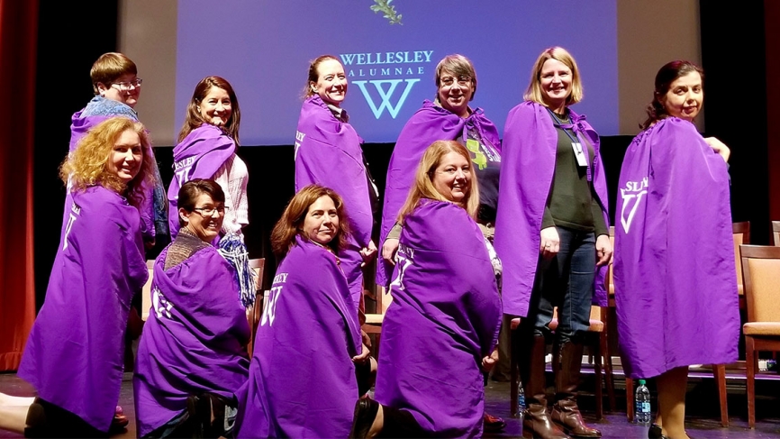 一群穿着紫色斗篷的妇女站在舞台上。