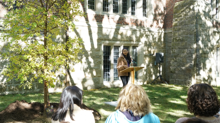 一个学生在一棵新种植的树旁边的一个讲台上讲话。