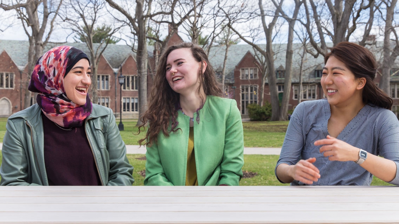 三个韦尔斯利沃森赢得了奖学金的学生在校园里坐着,笑了。