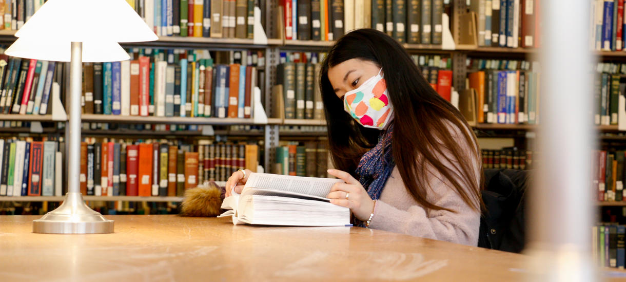 学生在图书馆读书在2020年秋天，戴着一个五颜六色的面具为自己和他人的covid保护。