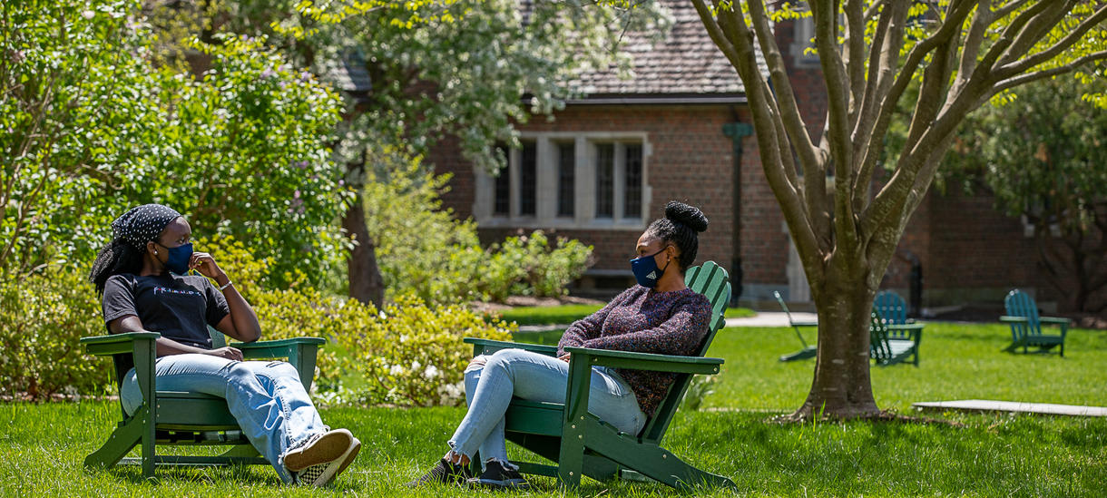 春日里，两个学生坐在门外，戴着口罩交谈。