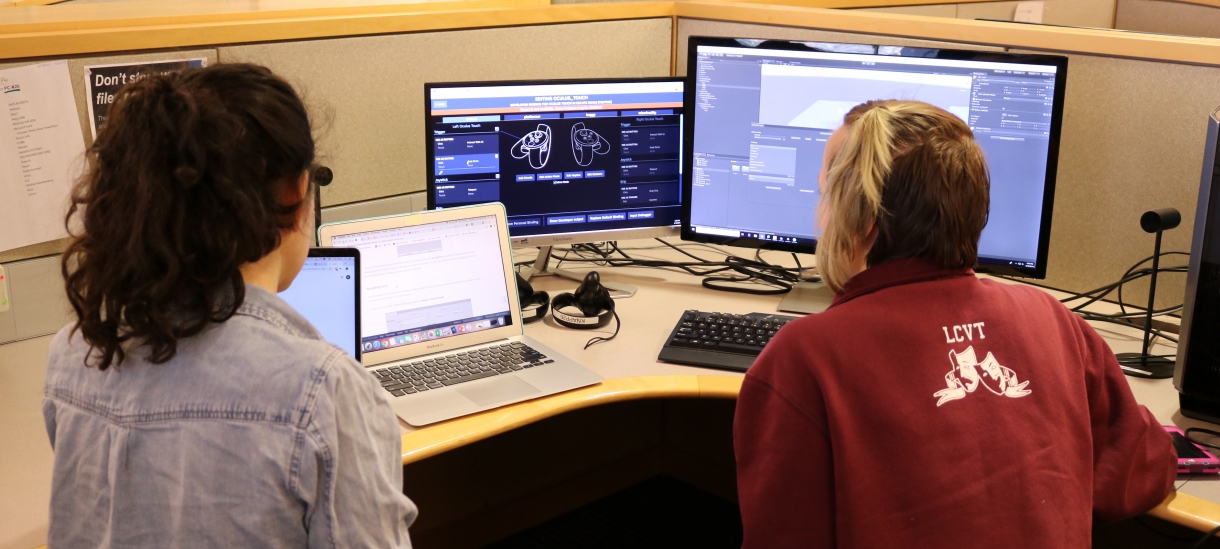 两个学生坐在和工作虚拟现实实验室计算机前面。