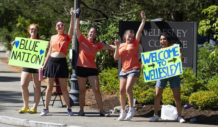 五名学生站在韦尔斯利（Wellesley）的入口处，挥舞着受欢迎的标志。