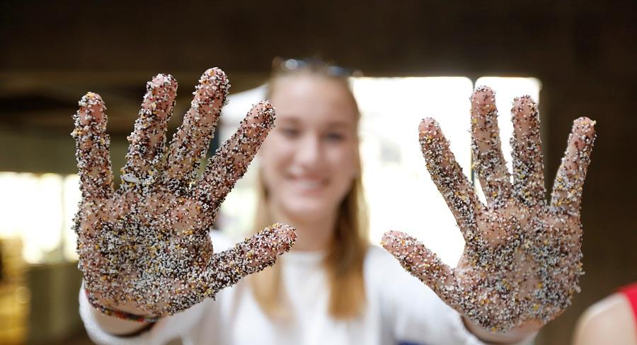 A Wellesley College student holds out her hands in front of her, covered in dyed sand